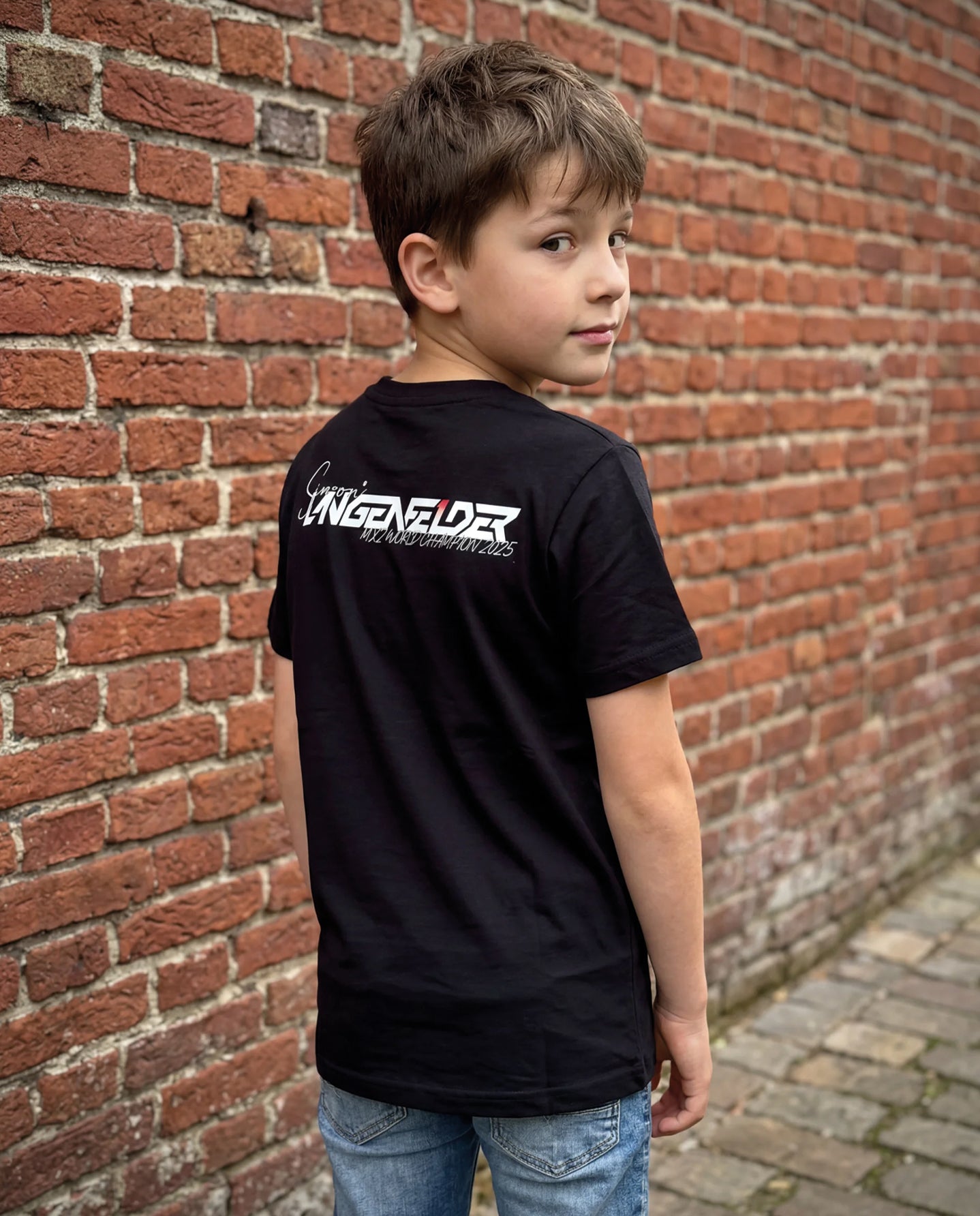 Rückansicht eines Kindes im schwarzen SL27 „Kids HomeGP Germany“ T-Shirt mit weißem „Simon Längenfelder MX2 World Champion 2025“-Print im oberen Rückenbereich.
