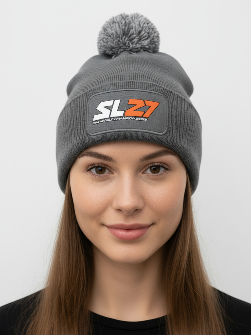 Graue SL27-Bommelmütze mit farblich passendem Pompon und schwarzem SL27-Gummipatch auf der Vorderseite, präsentiert vor hellem Hintergrund.