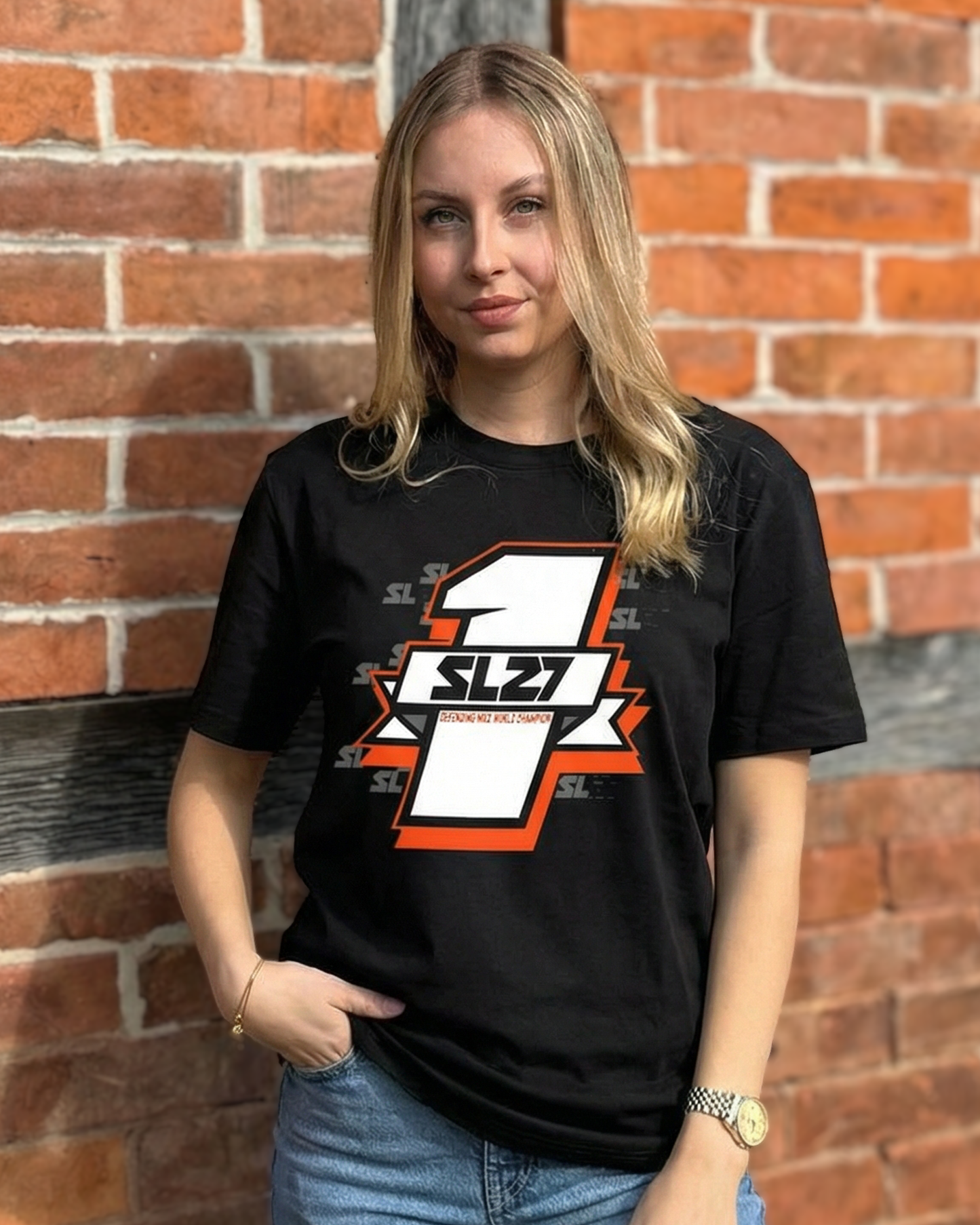Schwarzes SL27 T-Shirt „Number One“ mit großem Nummer-1-Design und SL27-Logo auf der Vorderseite, getragen vor einer Backsteinwand.