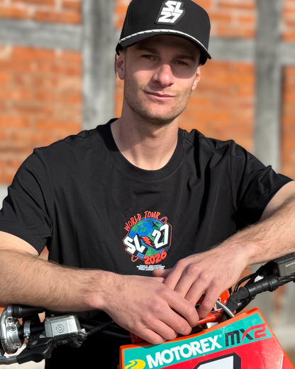 Schwarzes SL27 T-Shirt „World Tour 2026“ mit kleinem Globus-Logo auf der Brust, getragen von Simon Längenfelder auf seinem Motocross-Bike.